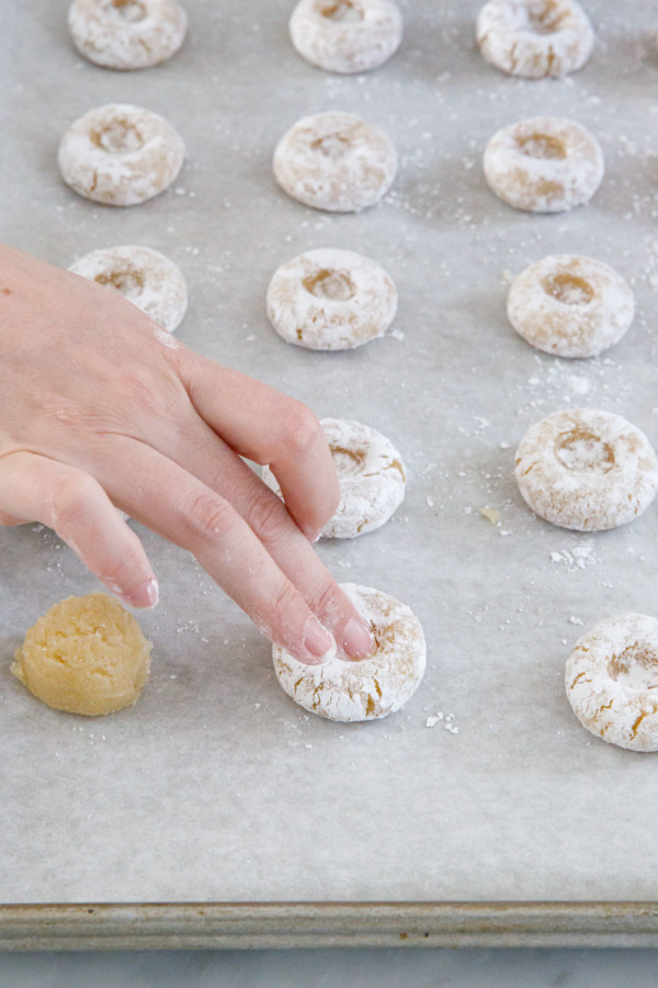 Using the fingertip to create small indentations in the unbaked thumbprint cookies