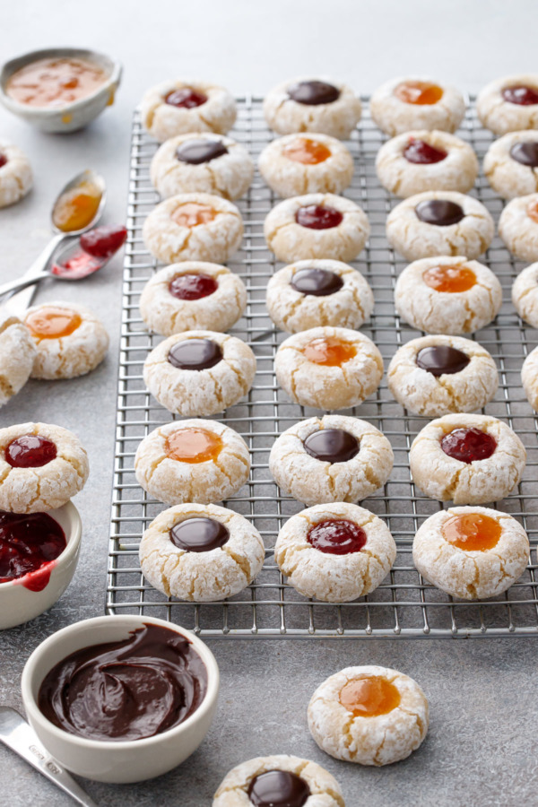 Rack of Amaretto Amaretti Thumbprints with three different filling options, with more cookies and ingredient bowls scattered around