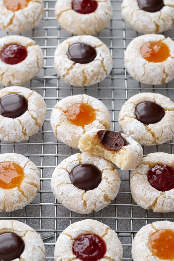 Wire rack with rows of Amaretto Amaretti Thumbprint cookies, one cookie with a bite out of it to show texture