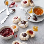 Amaretto Amaretti Thumbprint cookies on a gray background, with bowls of the various filling options messily scattered around