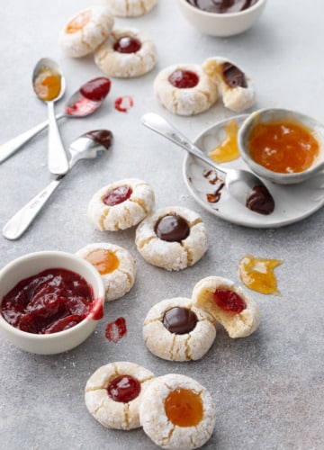 Amaretto Amaretti Thumbprint cookies on a gray background, with bowls of the various filling options messily scattered around