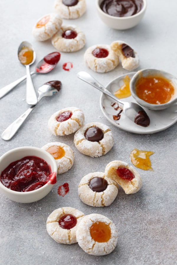 Amaretto Amaretti Thumbprint cookies on a gray background, with bowls of the various filling options messily scattered around