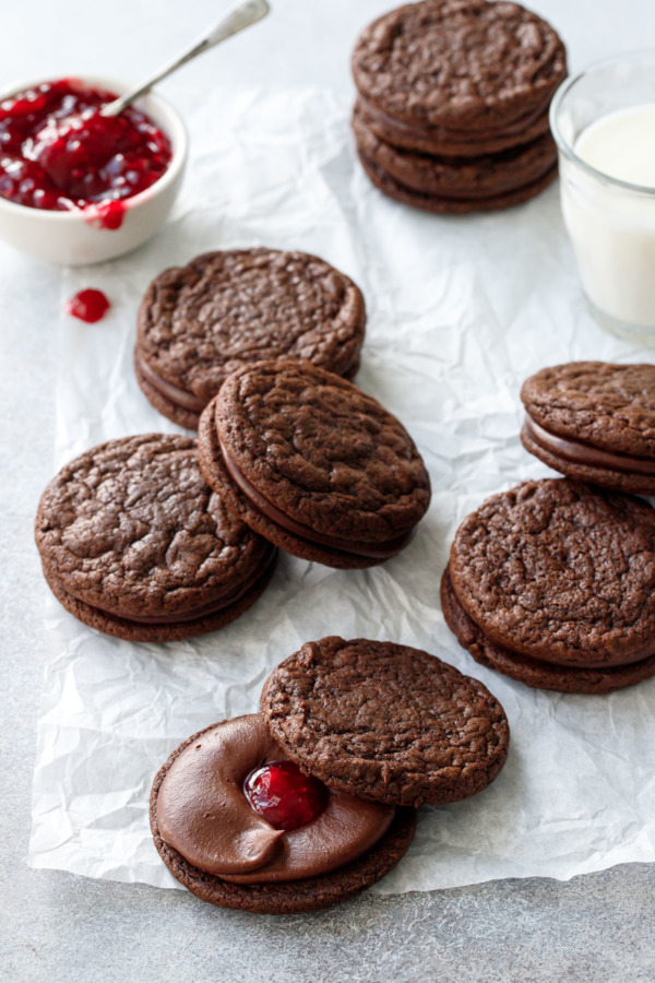 Crinkled parchment with Chocolate Raspberry Sandwich Cookies in progress, bowl of raspberry jam in the background.