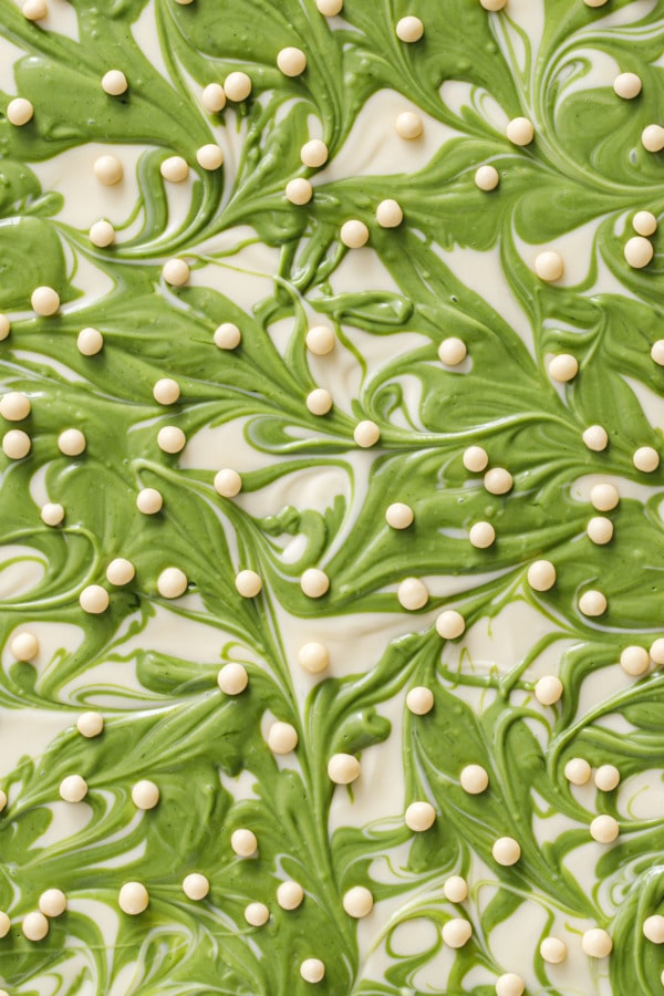 Overhead, closeup texture of Matcha White Chocolate Crunch Bark, showing swirls of green and white chocolate with dots of white chocolate crispearls