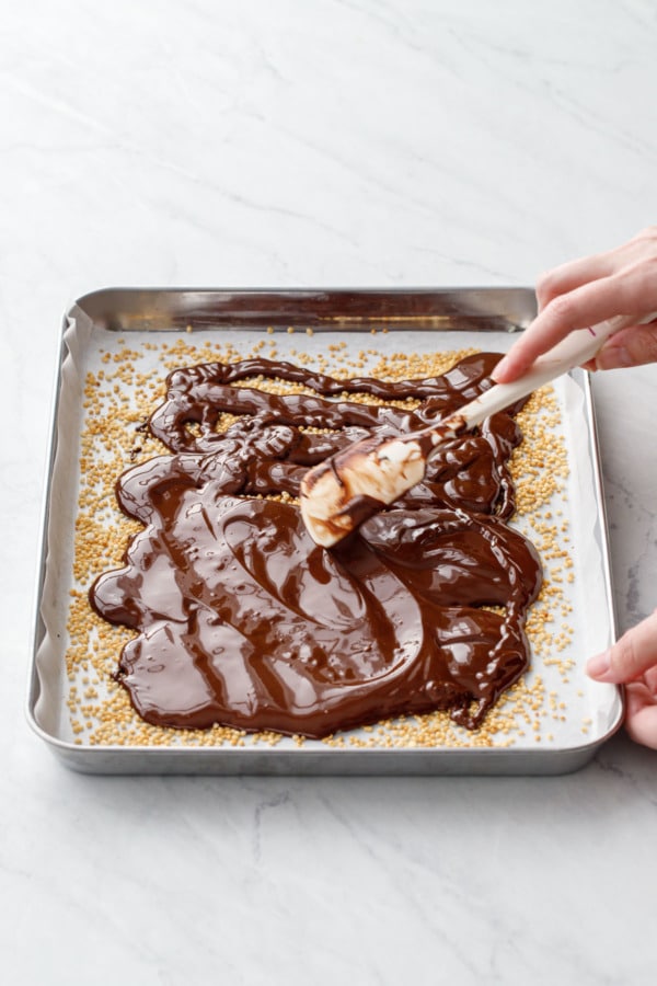 Spreading melted dark chocolate over top of puffed quinoa to make the bottom layer