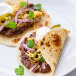 Two Easy Refried Black Bean Tacos on a white plate, topped with fresh cilantro