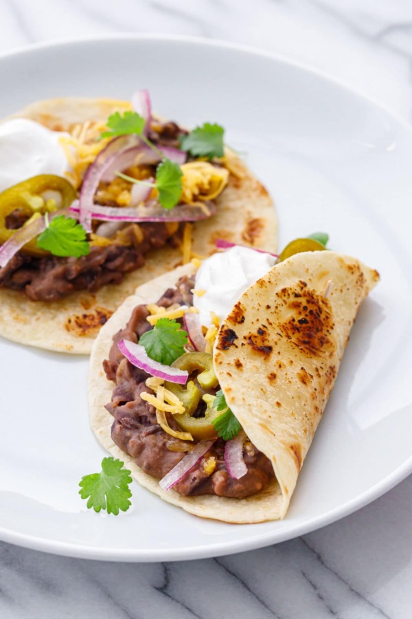 Two Easy Refried Black Bean Tacos on a white plate, topped with fresh cilantro