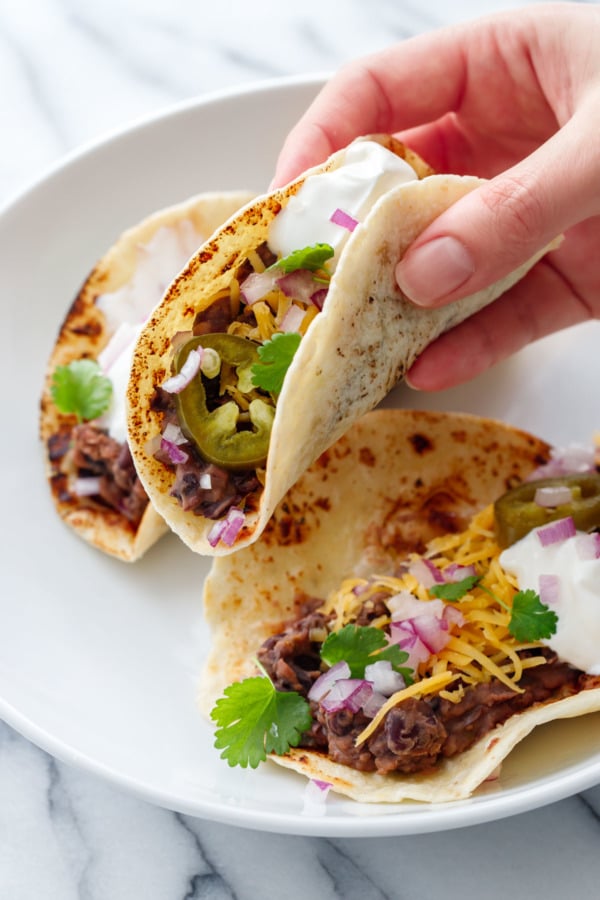 Hand lifting a Easy Refried Black Bean Taco, with toppings including a pickled jalapeno