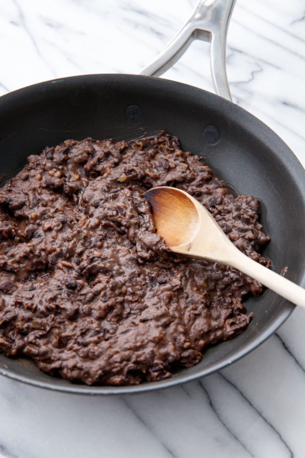 Pan of easy refried black beans and wooden spoon