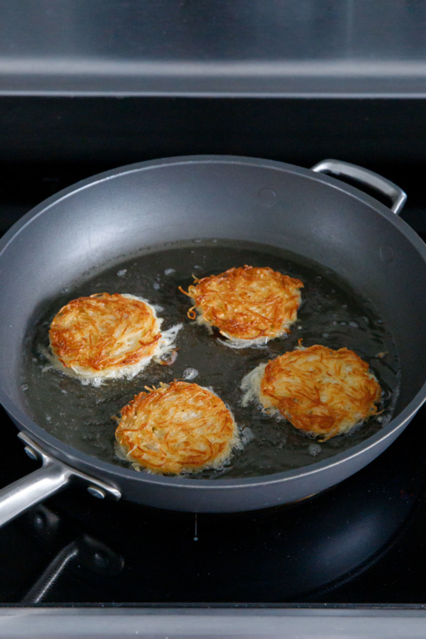 Four latkes in a nonstick skillet, after flipping to show the golden brown color