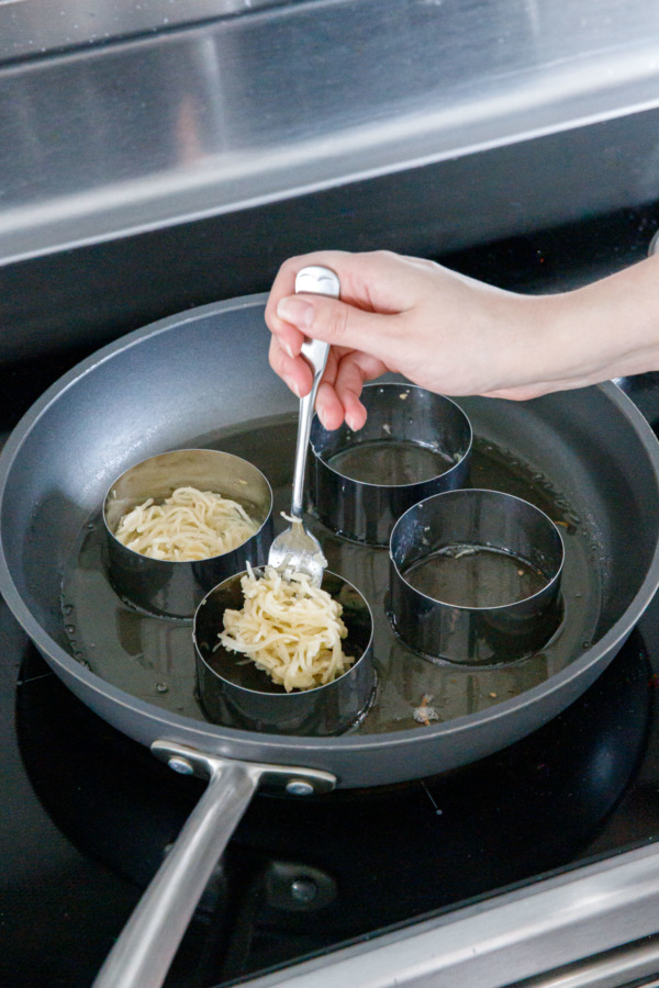 Dropping a forkful of potato latke mixture into ring molds in a hot skillet