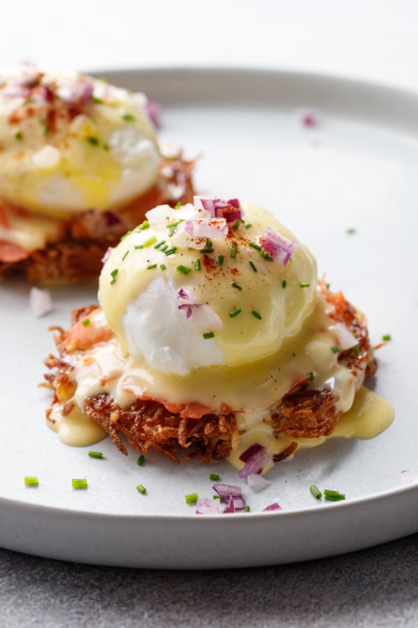 Closeup Latke Eggs Benedict, covered with thick butter yellow hollandaise sauce, garnished with chives and finely minced red onion.
