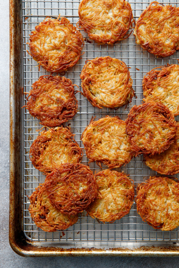 Perfectly round, golden brown latkes on a silver wire baking rack on baking sheet.