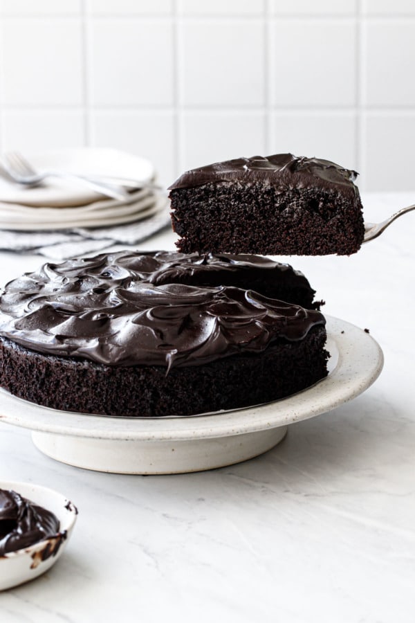 Lifting a cut slice out of a Sour Cream Chocolate Cake on a white cake stand