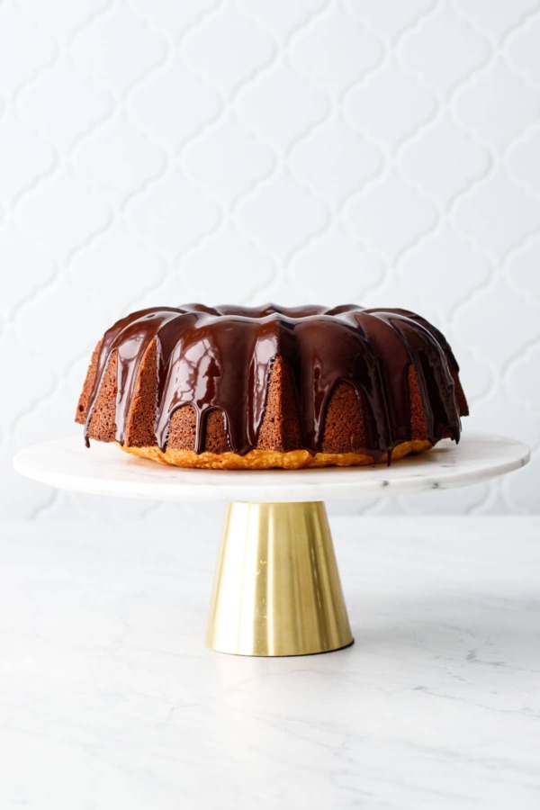 Almond Bundt Cake with Amaretto Ganache on a gold and marble cake stand with tile background