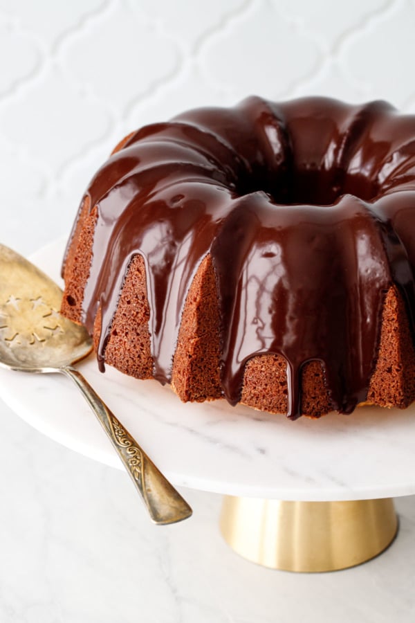 Almond Bundt Cake drizzled with Amaretto Ganache on a marble cake stand with gold cake server