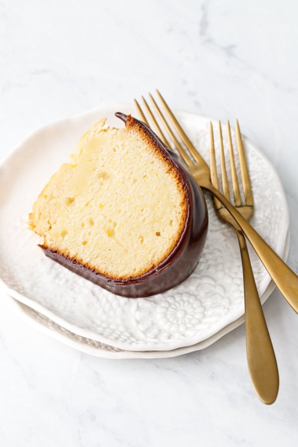 Slice of Almond Bundt Cake with Amaretto Ganache, with two gold forks on lacey white ceramic plates