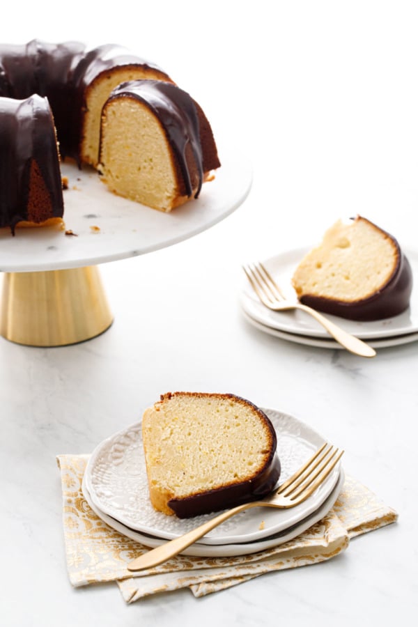 Slices of Almond Bundt Cake with Amaretto Ganache on white plates, with gold forks, and the rest of the cake on a marble cake stand in the background