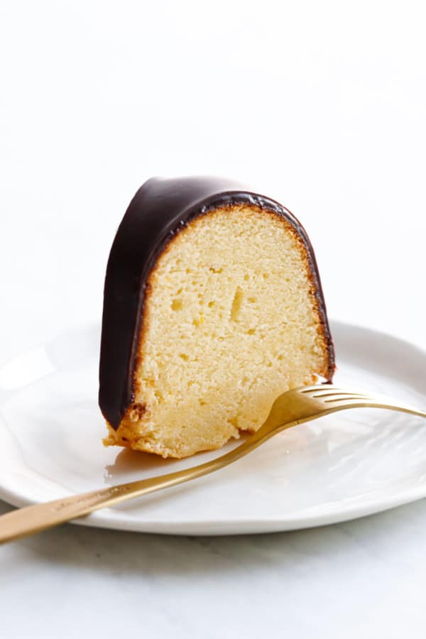 One slice of Almond Bundt Cake with Amaretto Ganache sitting on a white plate to show the closeup texture, gold fork
