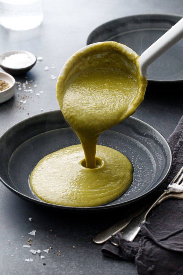 Pouring the pureed kohlrabi greens and leftover pulp (soup-like consistency) into a dark gray ceramic bowl