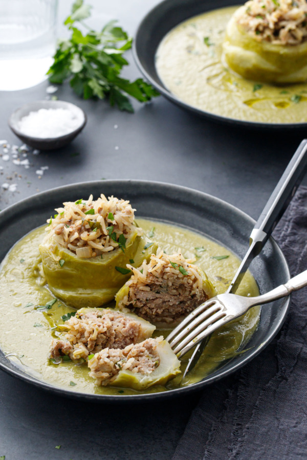 Hungarian Stuffed Kohlrabi in a dark gray bowl and fork and knife, with one bulb cut in half to show the pork and rice filling inside