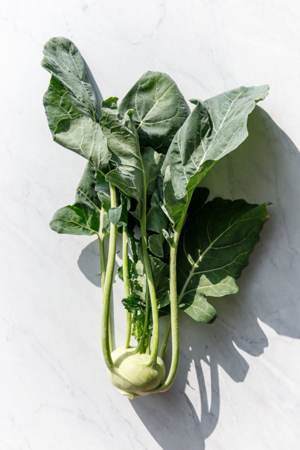 Single bulb of fresh kohlrabi, on a white marble background and harsh light and shadows