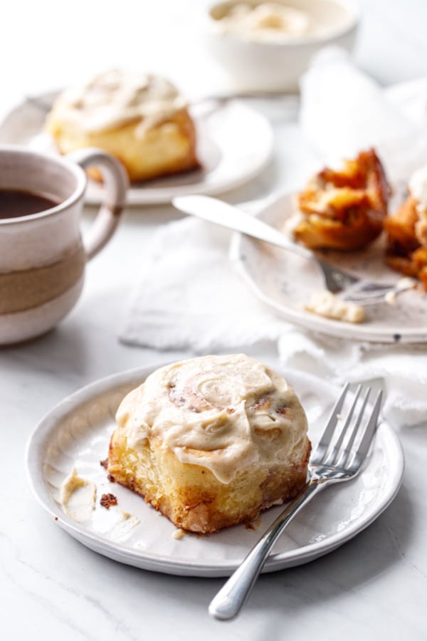 Plates of Brown Butter Cinnamon Rolls, cup of coffee and a white linen napkin