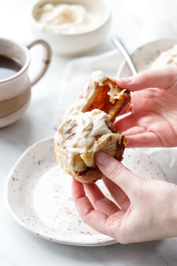 Pulling apart a warm Brown Butter Cinnamon Roll, showing the pillowy, gooey texture of the inside.