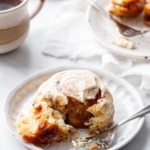 One Brown Butter Cinnamon Roll on a ceramic plate, with a forkful to show the pillowy texture.