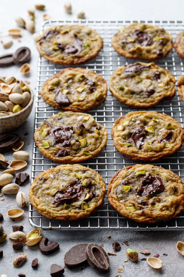 Wire rack with even rows of Salted Pistachio & Dark Chocolate Chunk Cookies, scattered bits of pistachio and dark chocolate scattered around