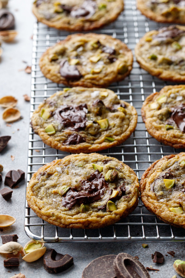 Wire rack with even rows of Salted Pistachio & Dark Chocolate Chunk Cookies, scattered bits of pistachio and dark chocolate scattered around