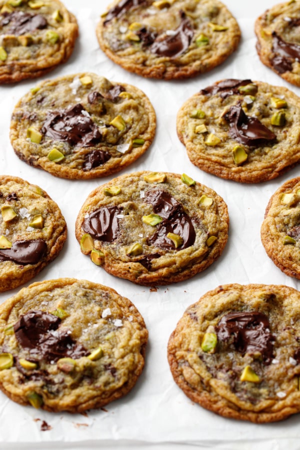 Staggered rows of Salted Pistachio & Dark Chocolate Chunk Cookies on crinkled white parchment