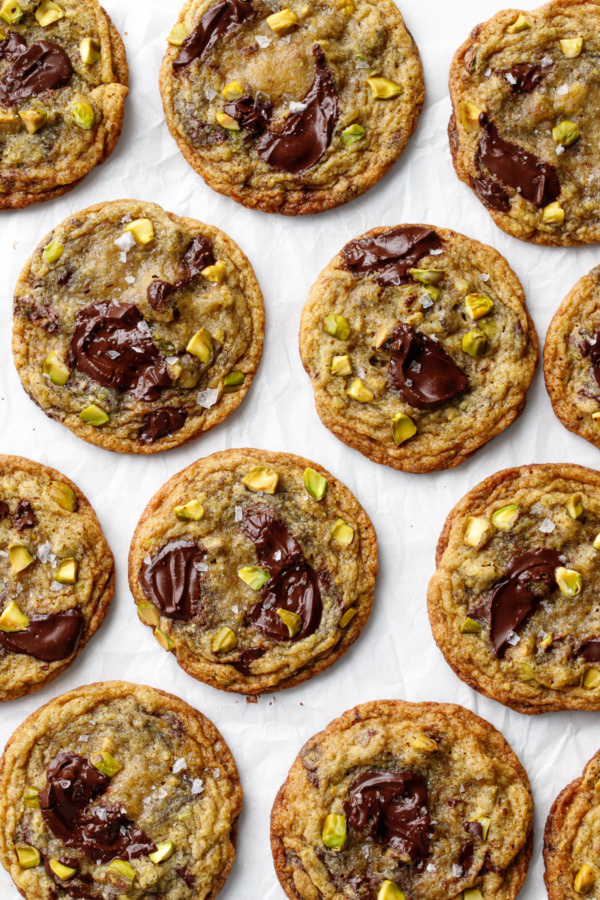 Overhead, staggered rows of Salted Pistachio & Dark Chocolate Chunk Cookies on crinkled parchment paper