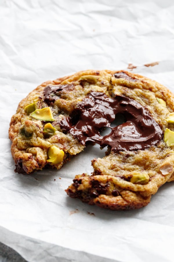 A single Salted Pistachio & Dark Chocolate Chunk Cookie broken in half to highlight the puddle of melted dark chocolate on top