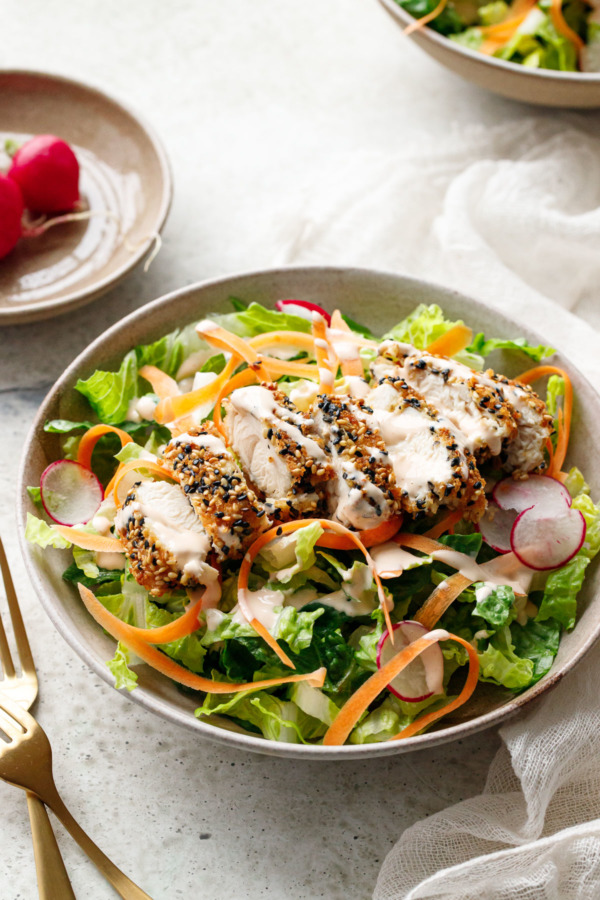 Ceramic bowl with romaine lettuce, shaved carrot, thinly sliced radish and sliced Panko Sesame Chicken Tender on top