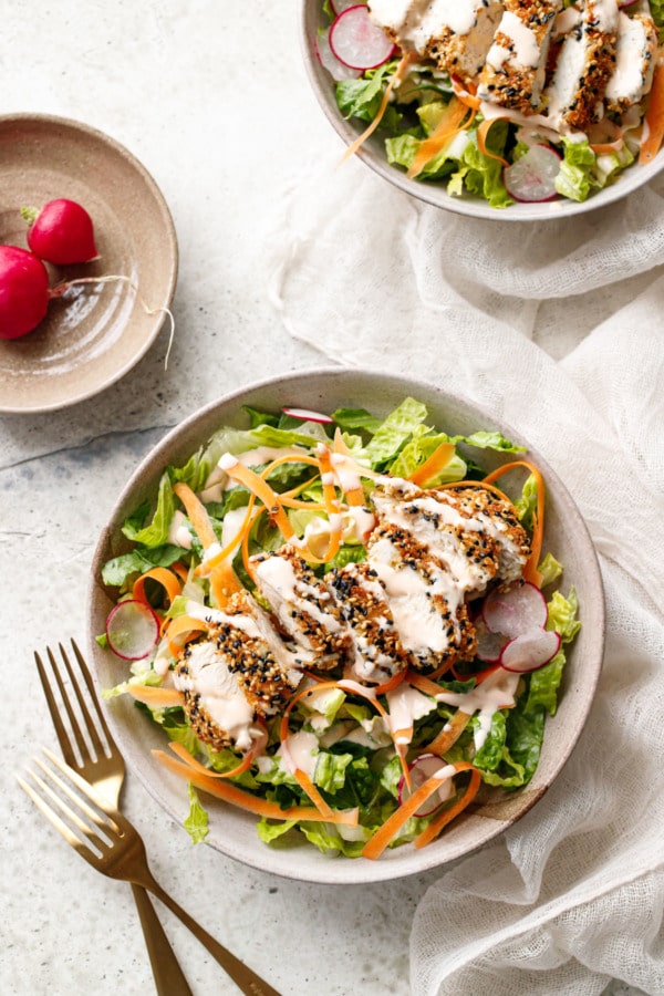 Overhead, two bowls with romaine lettuce, shaved carrot, thinly sliced radish and sliced Panko Sesame Chicken Tender on top