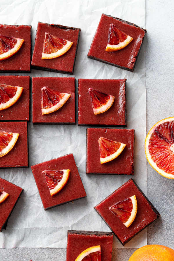Overhead, cut squares of Blood Orange Curd Brownies on a piece of crinkled white parchment paper.