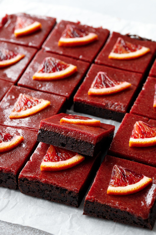 Neat grid of Blood Orange Curd Brownies cut into squares, one piece propped up to showcase the perfectly defined layers of brownie and deeply-colored blood orange curd.