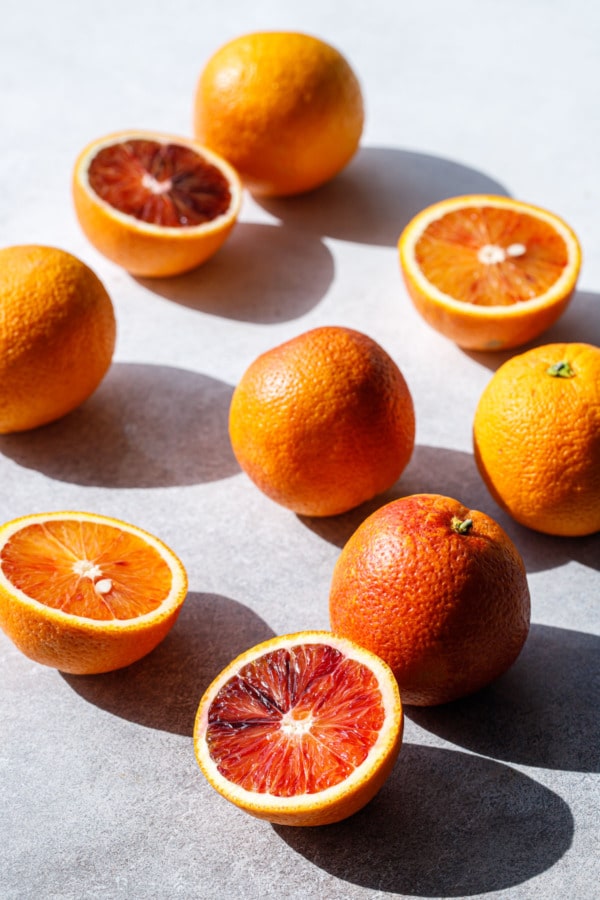 Still life shot of blood oranges on a gray background, with direct light and harsh long shadows.