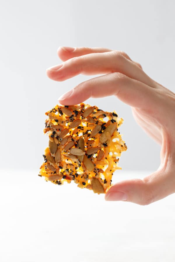 Hand holding one seeds and cheese cracker up to the light, to show the holey texture