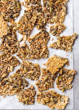 Overhead roughly broken pieces of Seeds and Cheese Crackers on a piece of parchment