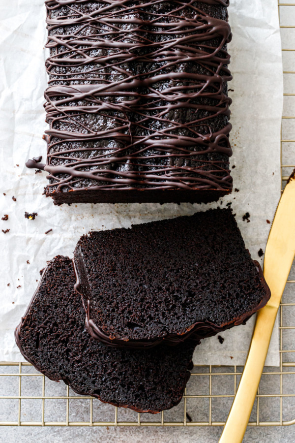 Overhead, two slices of Chocolate Olive Oil Loaf Cake with a drizzled chocolate glaze, gold knife.