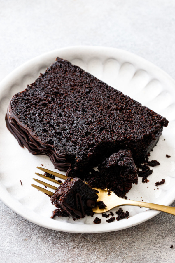 Closeup, slice of Chocolate Olive Oil Loaf Cake on a plate, with a piece on a fork to show the texture