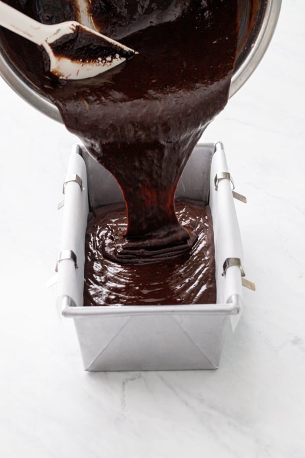 Pouring the thin chocolate batter into a parchment-lined loaf pan.