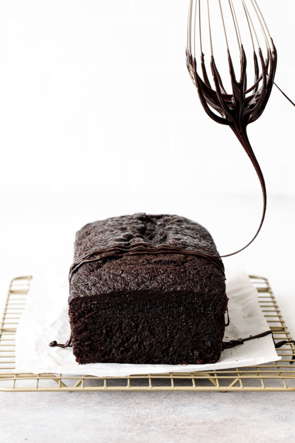 Whisk drizzling the Chocolate Olive Oil Loaf Cake with a chocolate glaze.