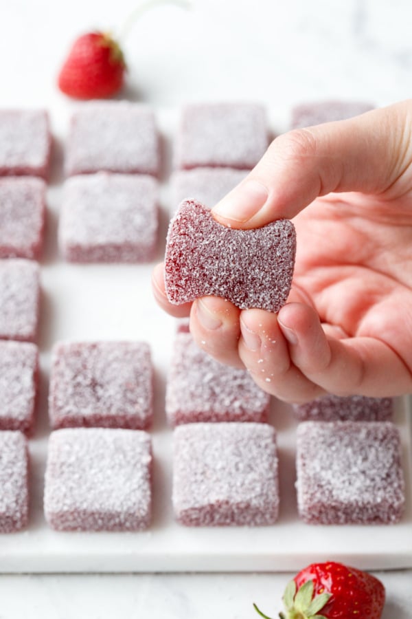 Squeezing a square piece of Homemade Sour Strawberry Gummy candy to show texture (frame 2).