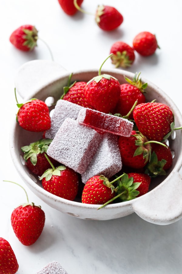 Berry bowl with strawberries and Homemade Sour Strawberry Gummies, one with a bite out of it to show texture.