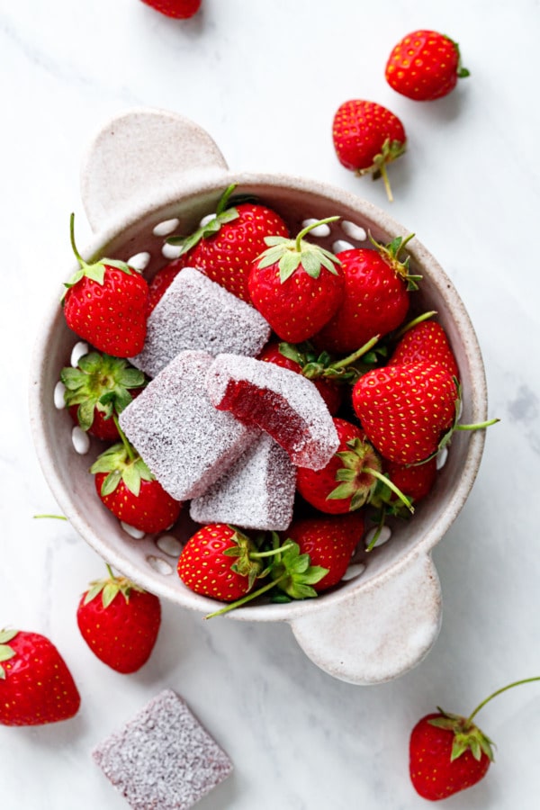 Overhead, berry bowl filled with strawberries and a few Homemade Sour Strawberry Gummy candies on a marble background