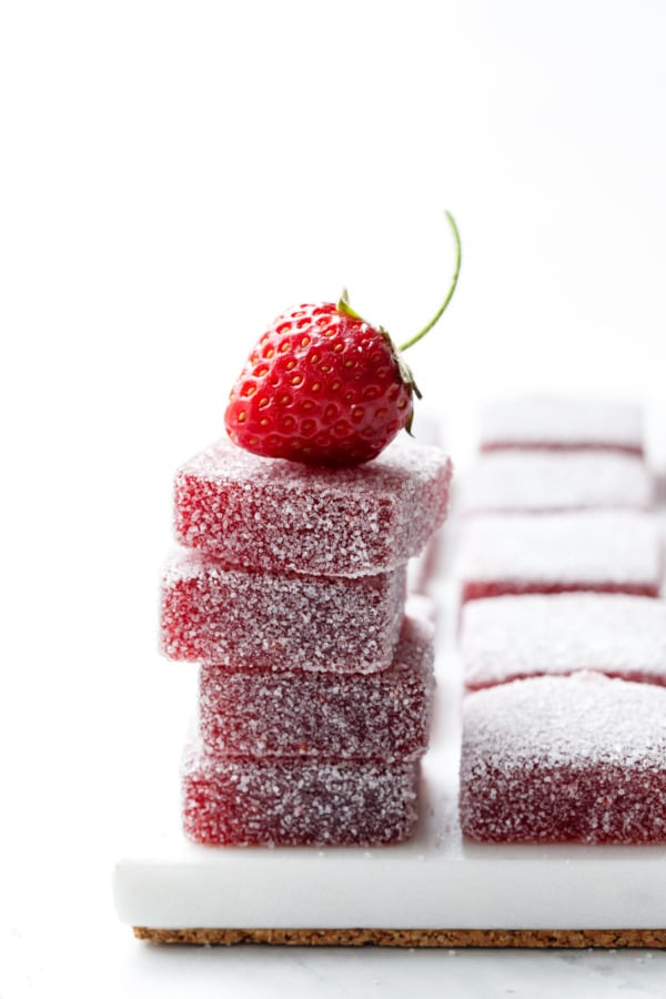 Backlit stack of Homemade Sour Strawberry Gummies with a single stemmed strawberry balanced on top.