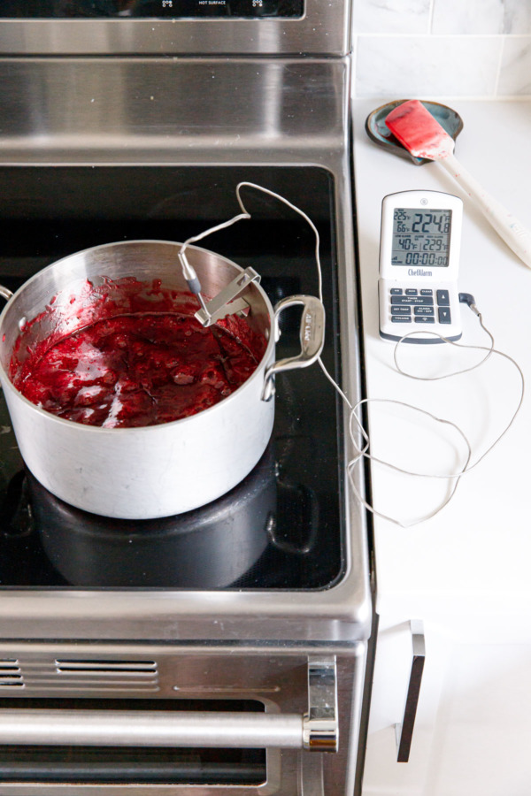 Saucepan on the stove filled with bubbling fruit mixture, with a probe thermometer off to the side.